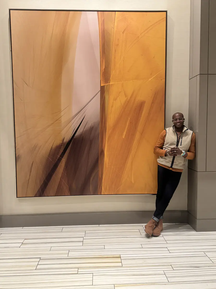 Maurice Howell stands beside a large amber abstract artwork.