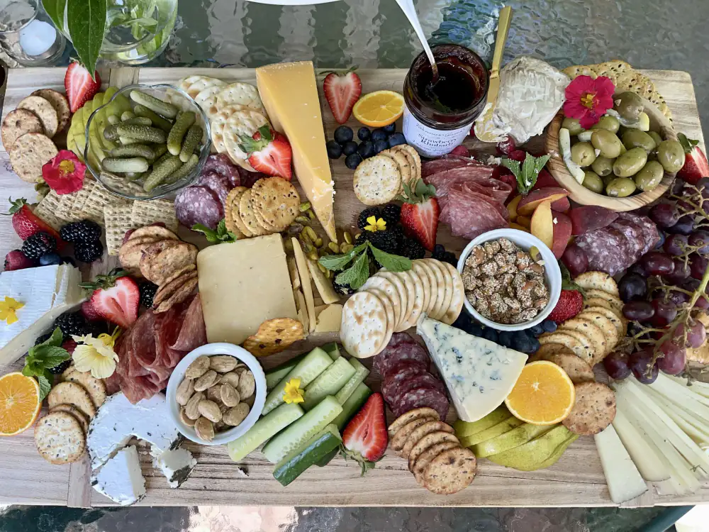 A grazing board arranged with cheeses, cured meats, crackers, fruit, olives, nuts, and edible flowers.